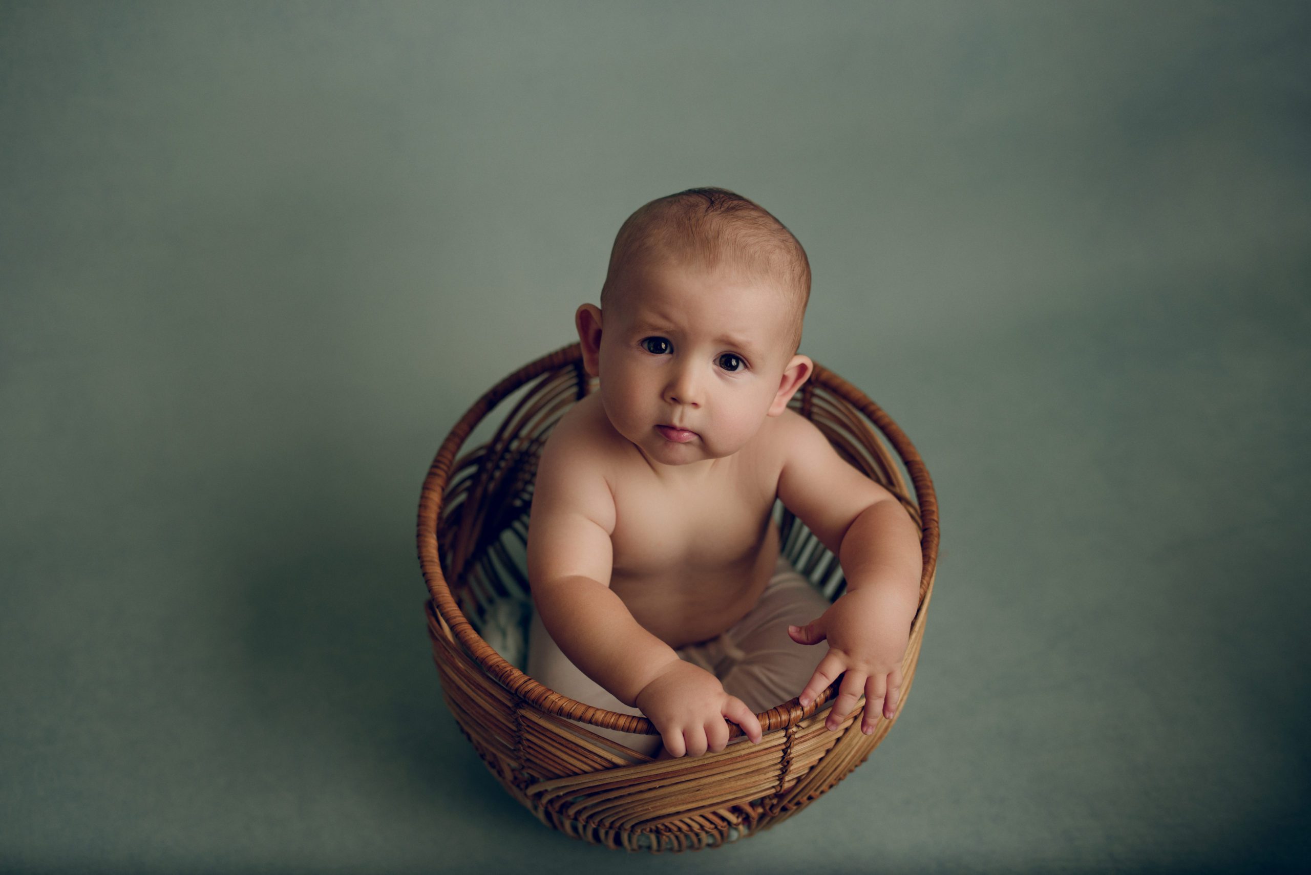 baby in a rattan basket on a teal background