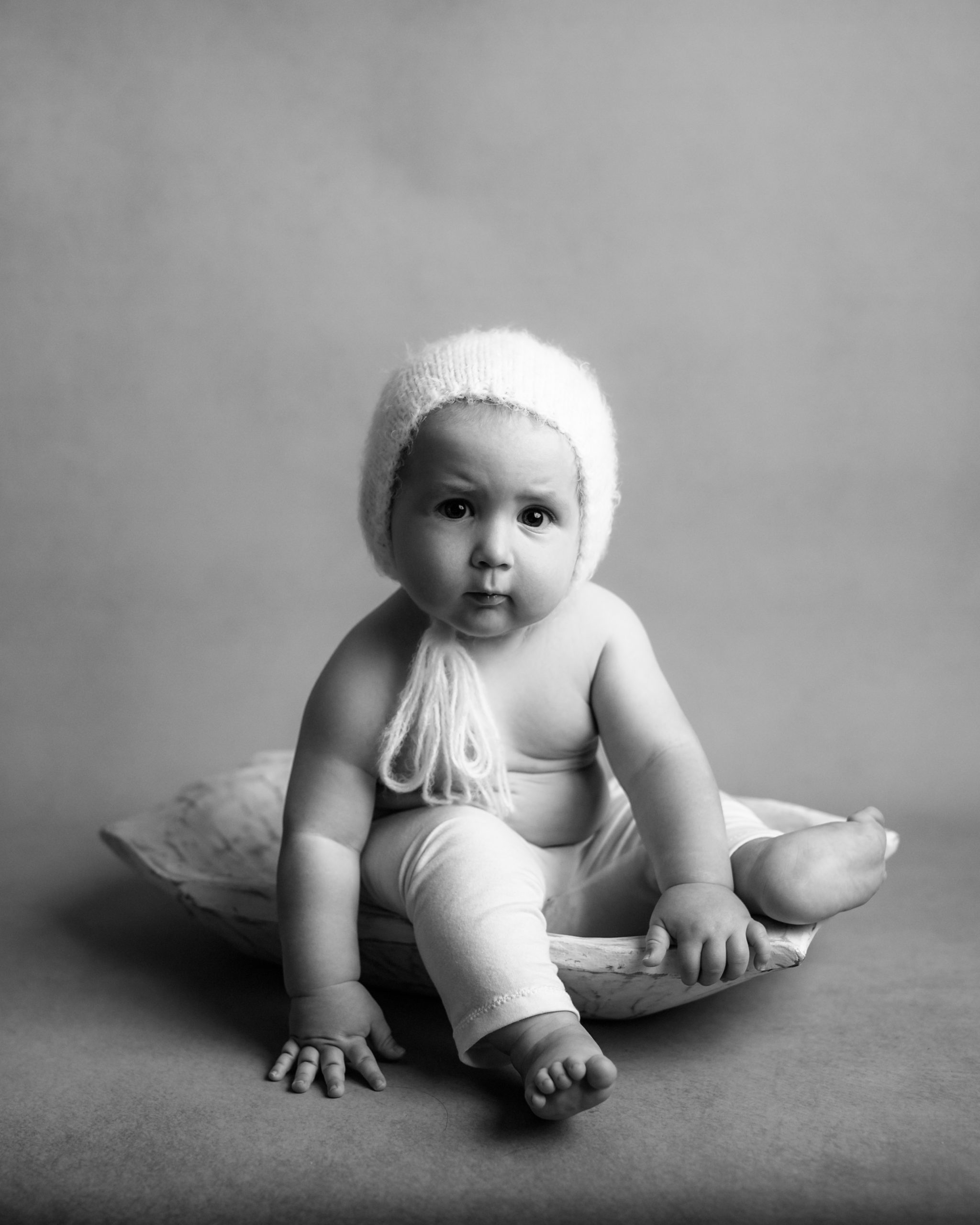 baby sitting in a bowl with white pants and bonnet in black and white