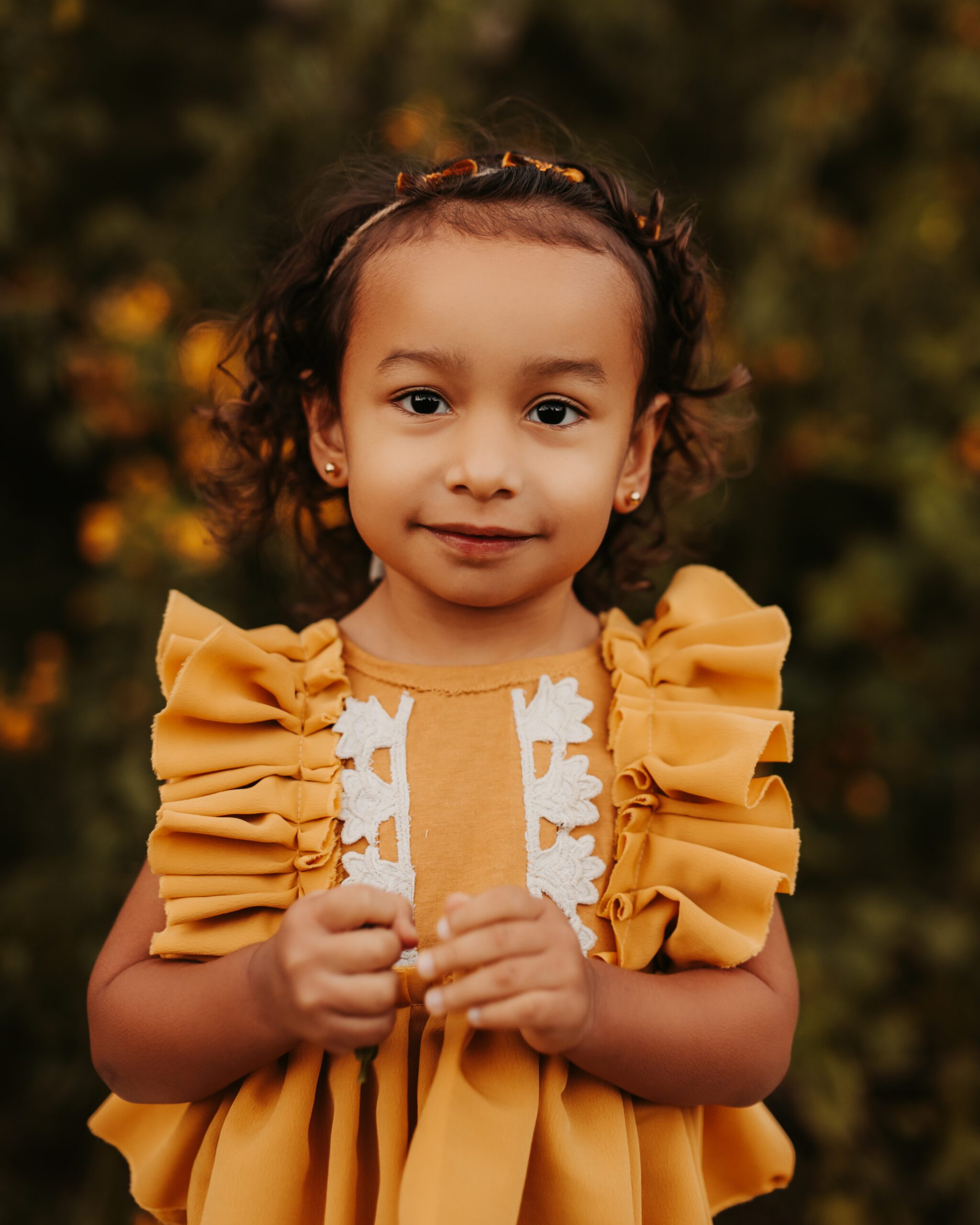 toddler girl wearing yellow ruffled dress standing in front of yellow flowers